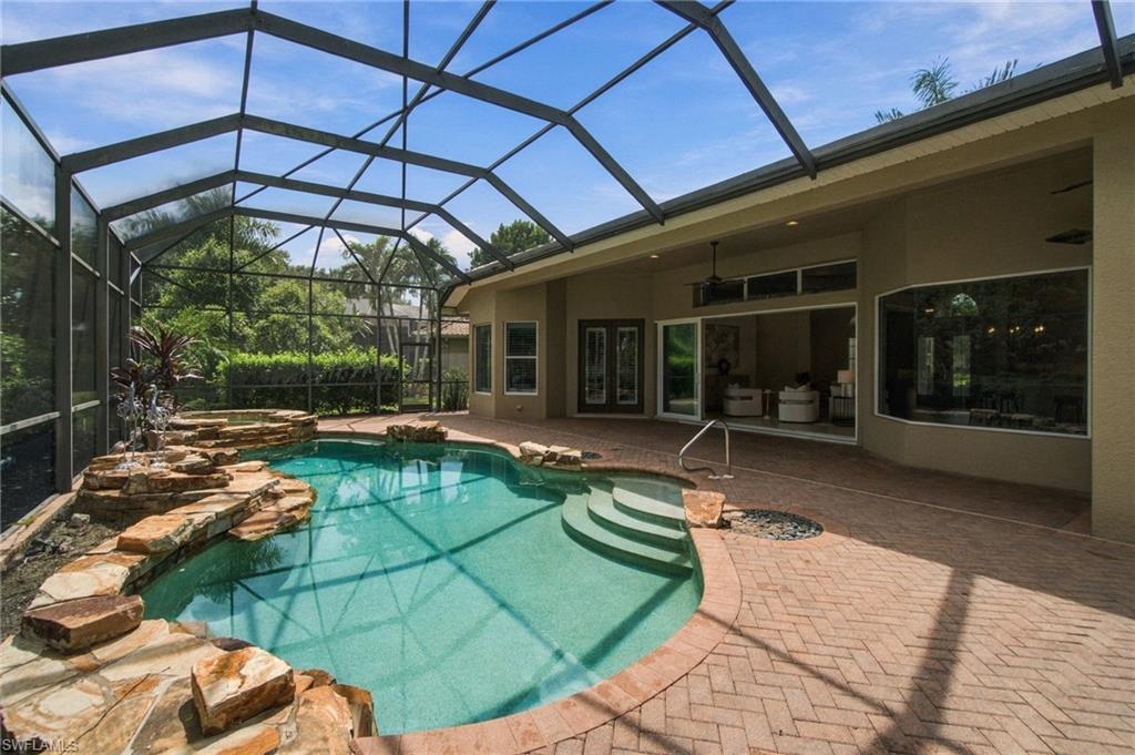 Screened backyard pool with a rock waterfall and curved entry steps beside the house.