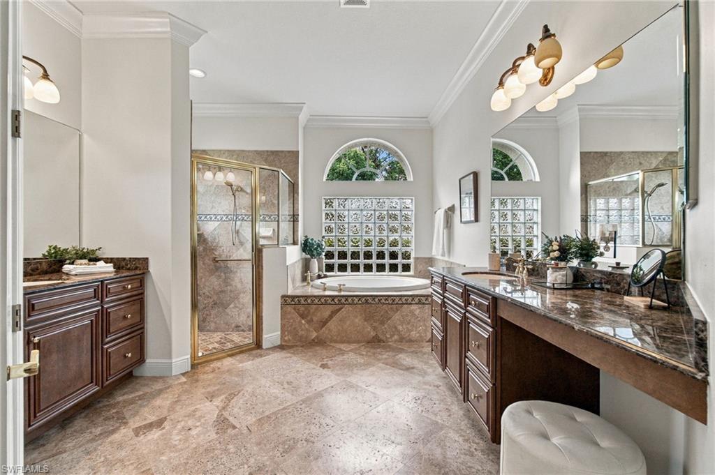 Primary bathroom with dark wood vanities, a glass shower, and a soaking tub beneath an arched window.