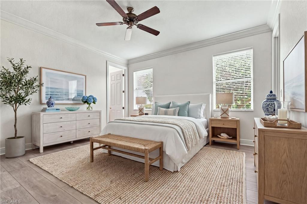 Staged bedroom with a white bed, pale wood furniture, and a woven rug.