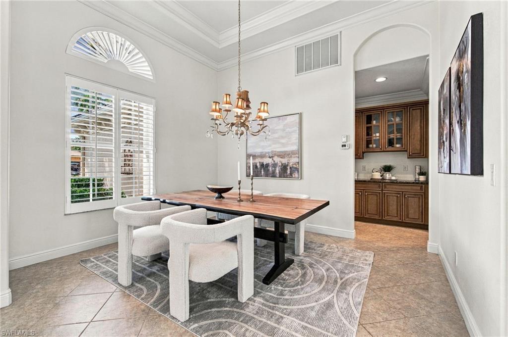 Dining room with a wood-top table, white chairs, chandelier, and plantation shutters.