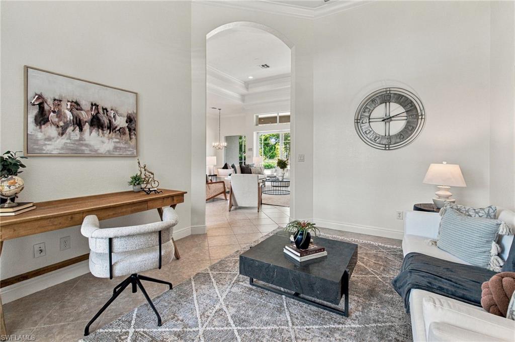 Staged living room with a desk, horse artwork, and an arched opening to a bright sitting area.