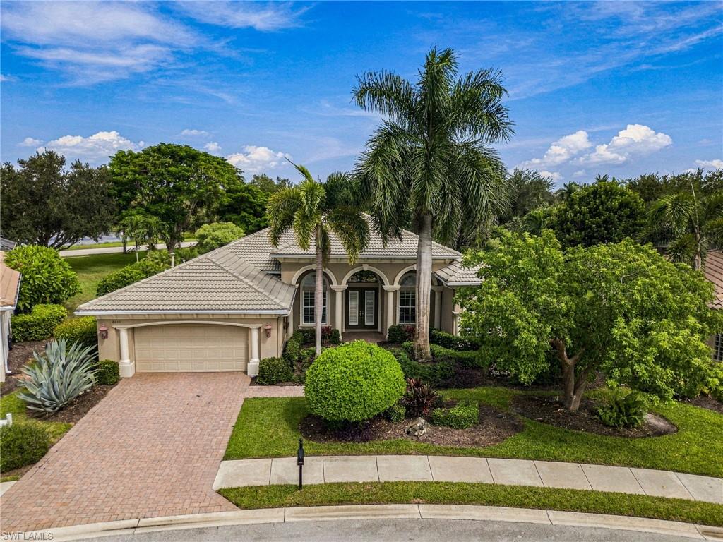 Florida home with an arched entry, two-car garage, brick driveway, and tall palm trees.