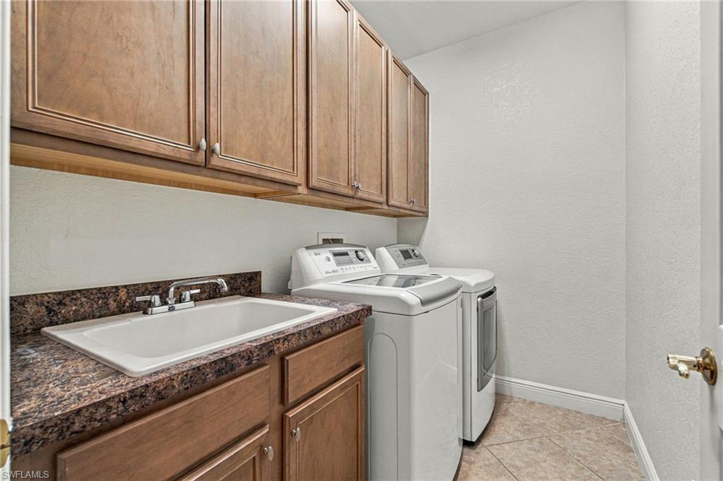 Laundry room with wood cabinets, a speckled countertop, utility sink, washer, and dryer.