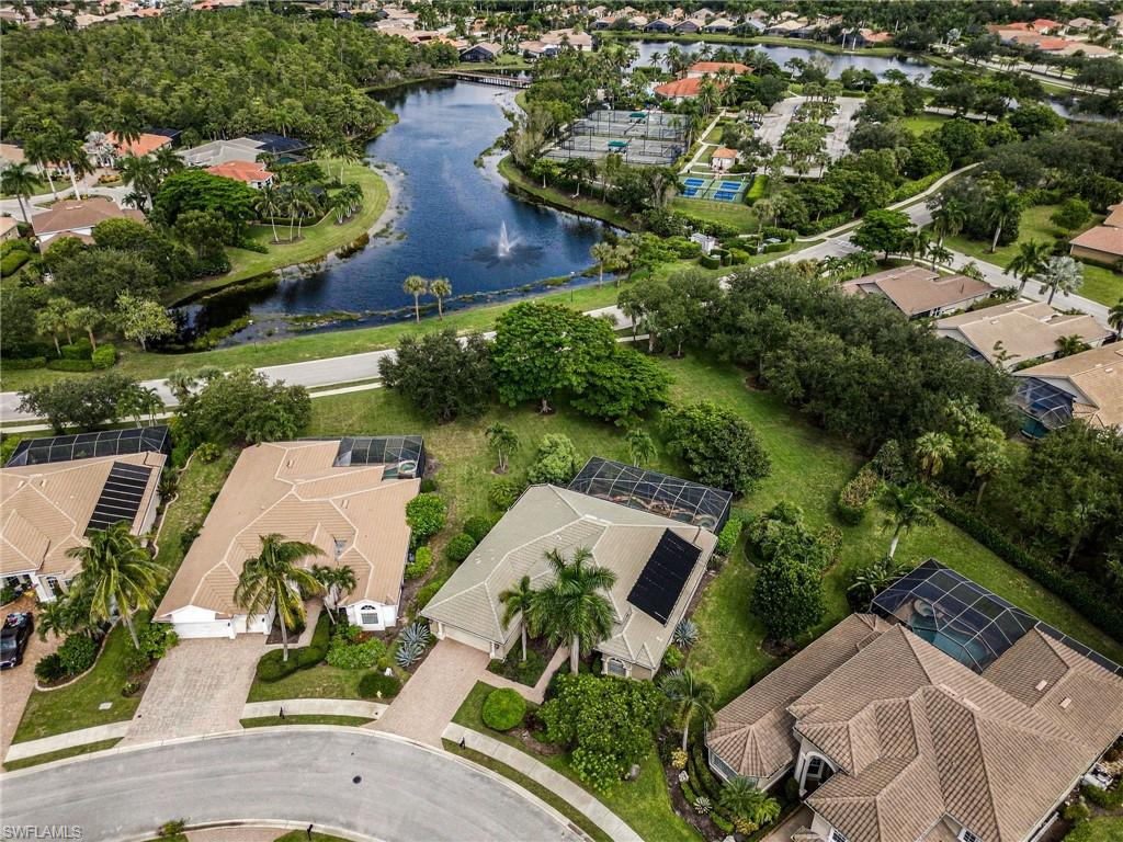 Aerial view of homes beside a lake with a fountain and tennis courts.