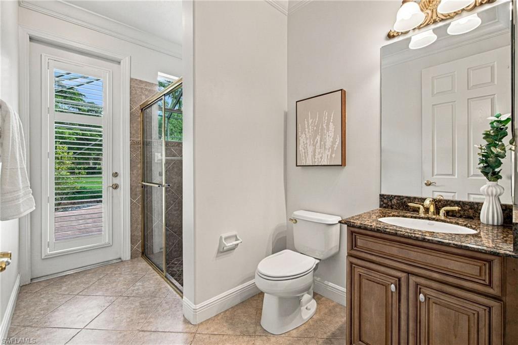 Bathroom with a wood vanity and stone counter beside a glass shower and louvered door.