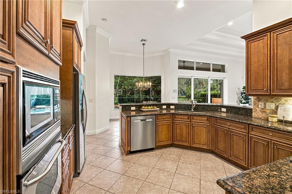 Kitchen with wood cabinets, granite counters, stainless appliances, and windows overlooking a green yard.