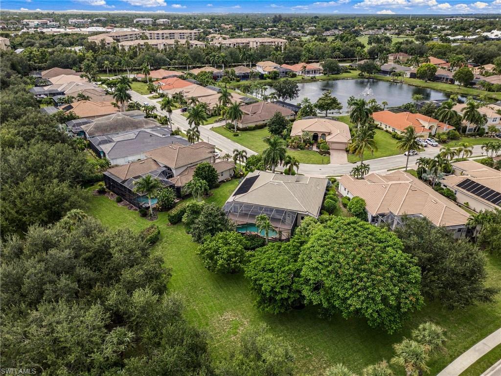 Aerial view of homes around a pond, with screened lanais and a tree-lined green space in the foreground.