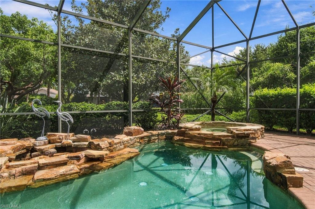 Screened pool with a raised stone spa, tropical landscaping, and flamingo ornaments.