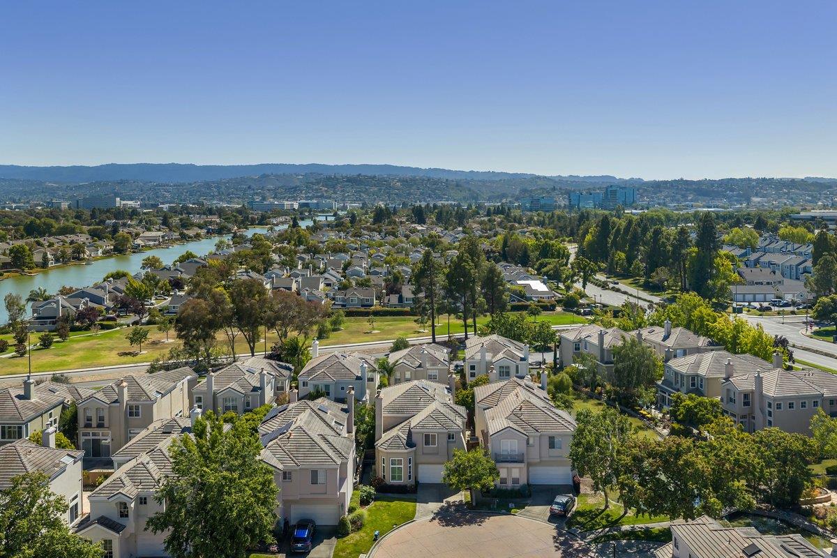 Aerial view of suburban homes beside a winding waterway, with green space and distant hills.