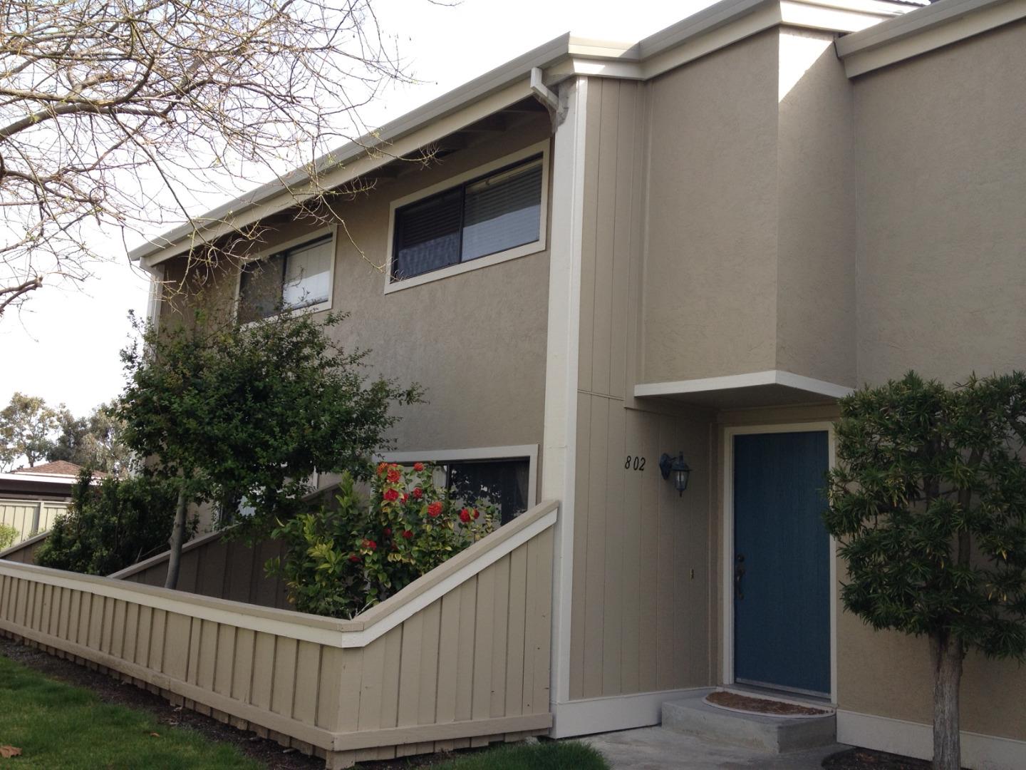 Beige two-story residence with a blue front door, fenced garden, and red flowers.