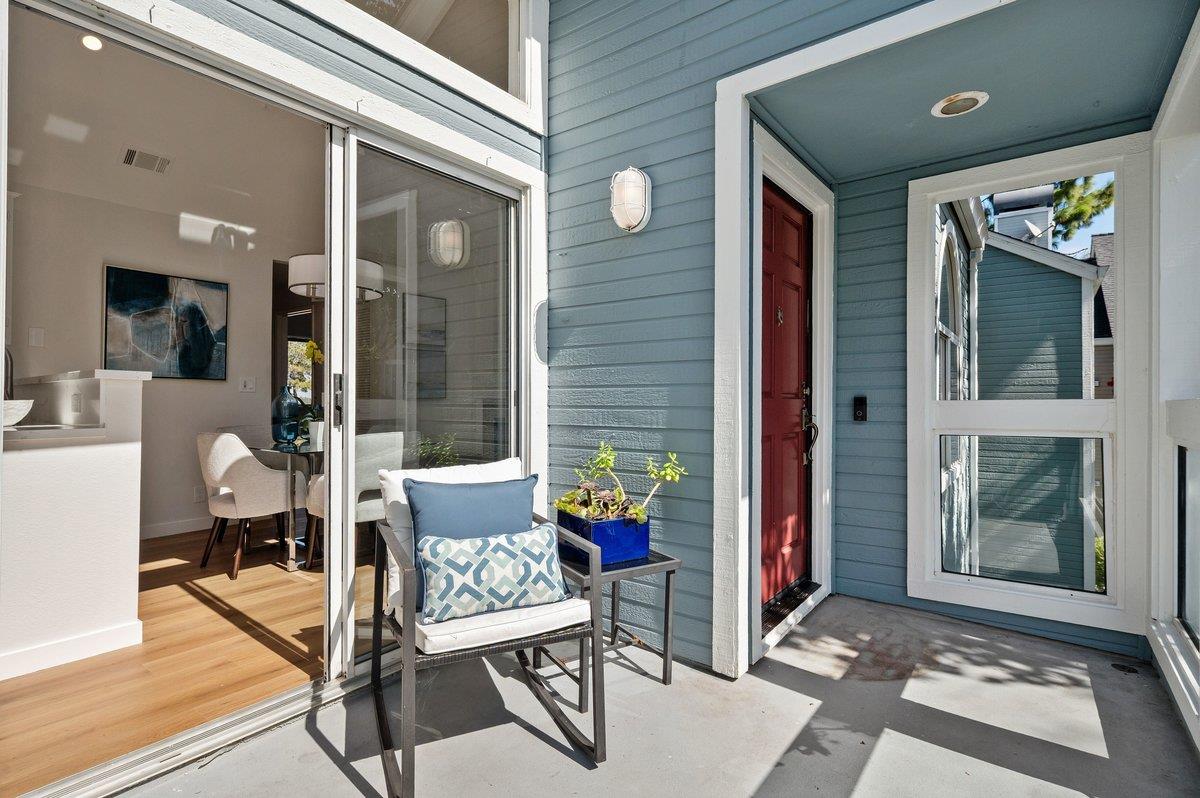 Covered home entry with a red door, blue siding, and a patio chair beside sliding glass doors.