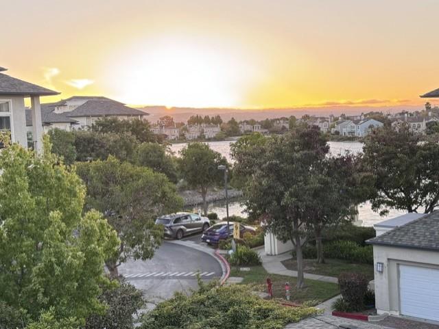 Residential neighborhood with distant water and trees under a golden sunset sky.
