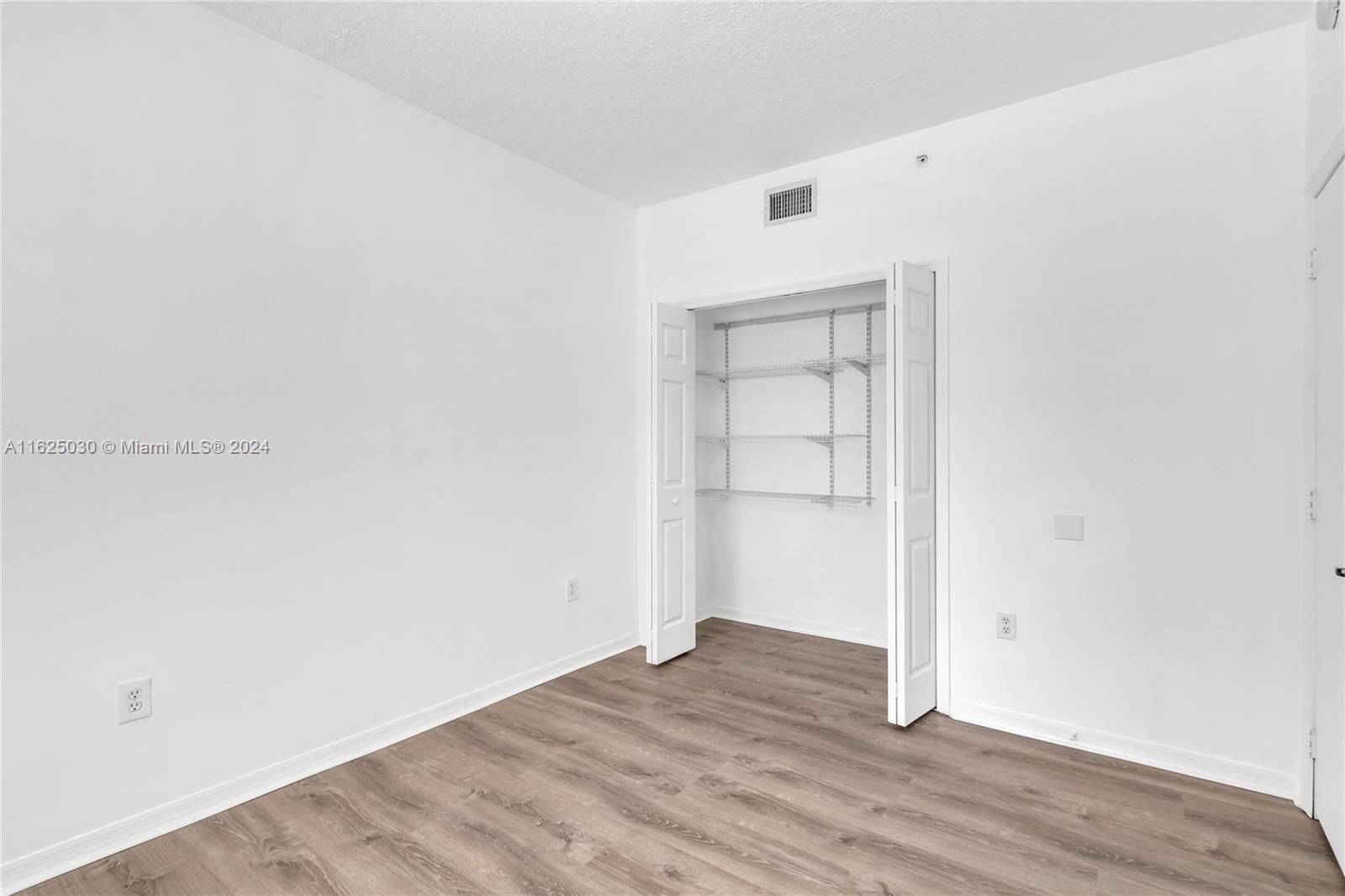 Empty bedroom with wood-look flooring and an open closet with wire shelving.