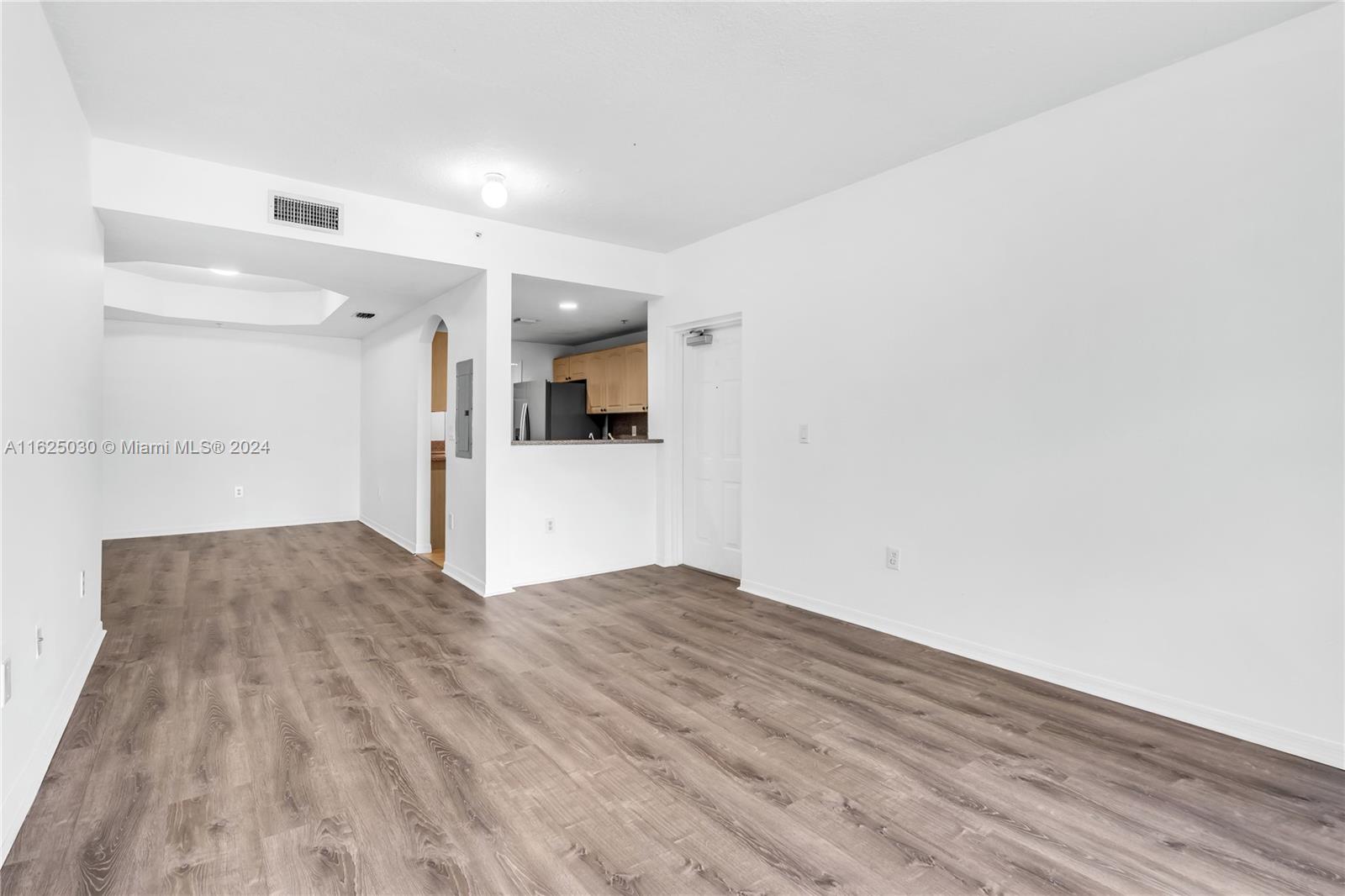 Vacant living and dining area with wood-look floors and an open kitchen.