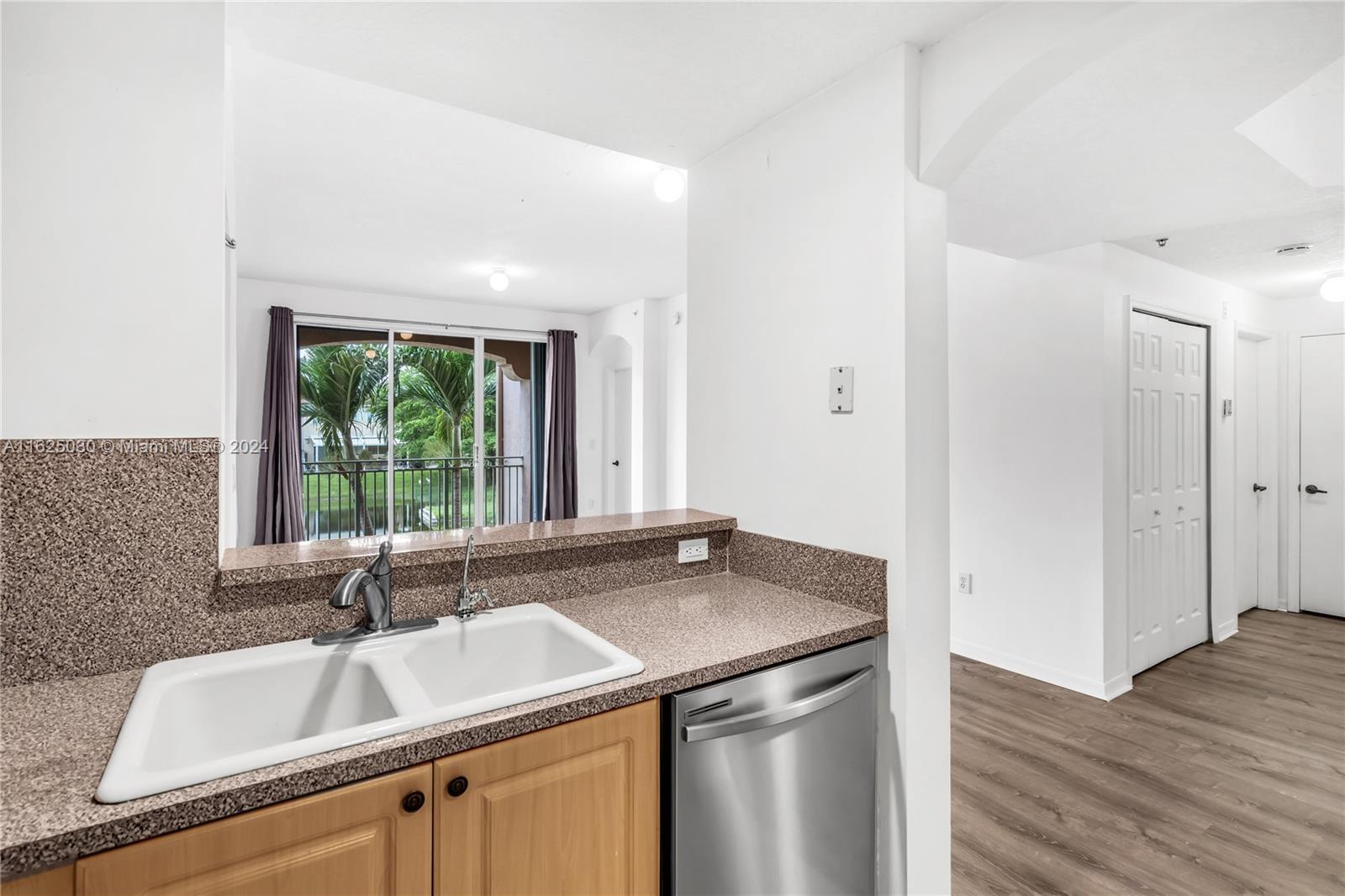 Kitchen with double-basin sink, stainless dishwasher, and sliding doors overlooking greenery.