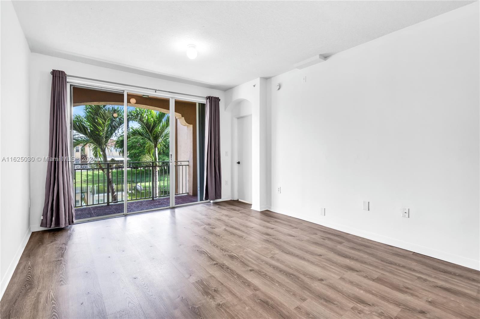 Vacant living room with wood-look floors and sliding doors to a palm-lined balcony.