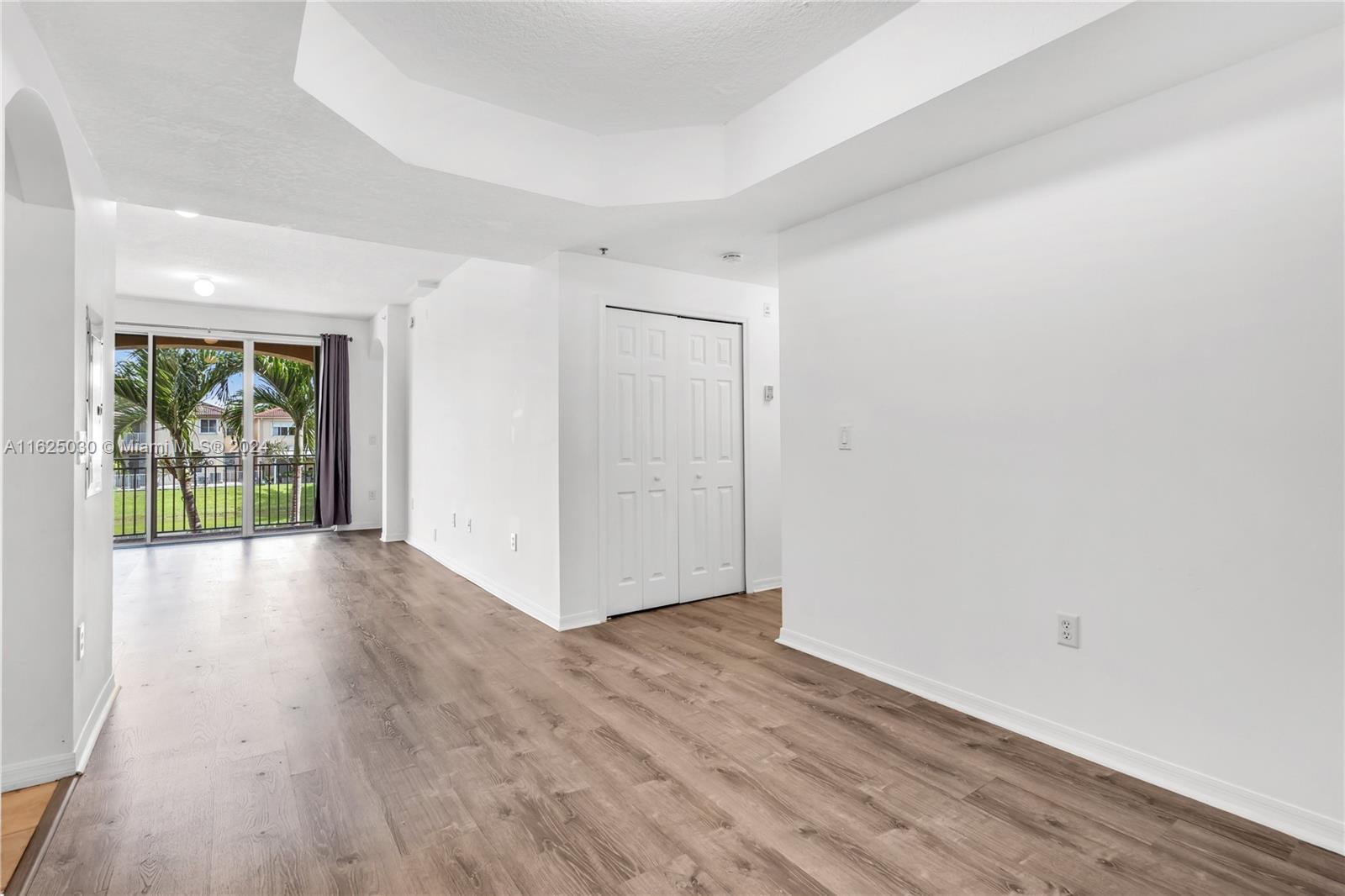 Empty living room with wood-look floors and sliding doors opening to a palm-lined balcony.