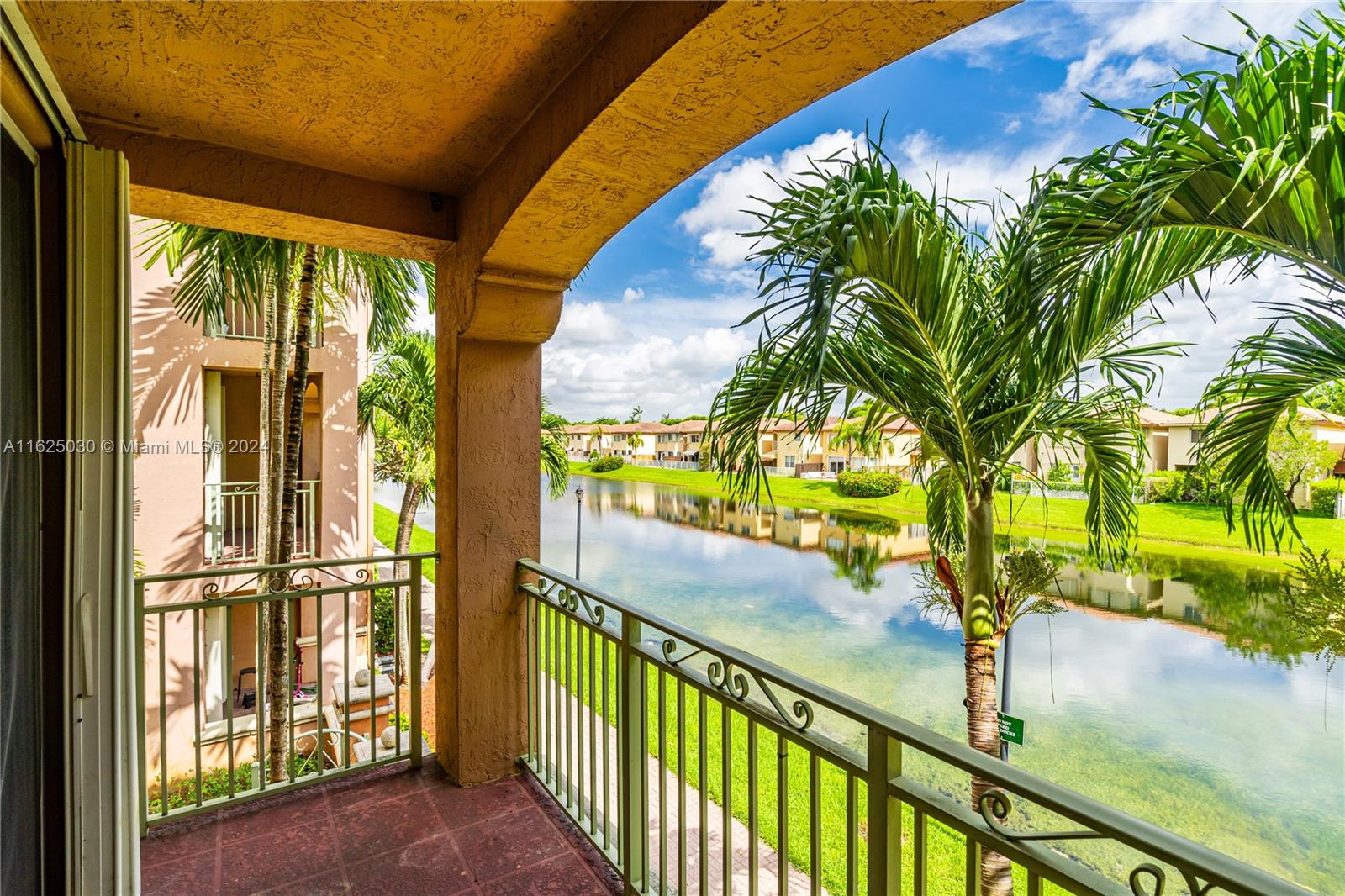 Apartment balcony overlooking a lake, with palm trees and homes across the water.