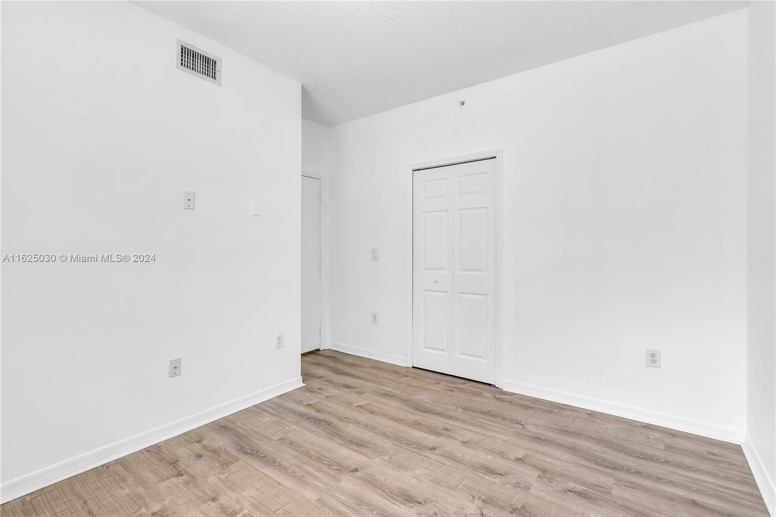 Empty room with white walls, a double-door closet, and wood-look flooring.