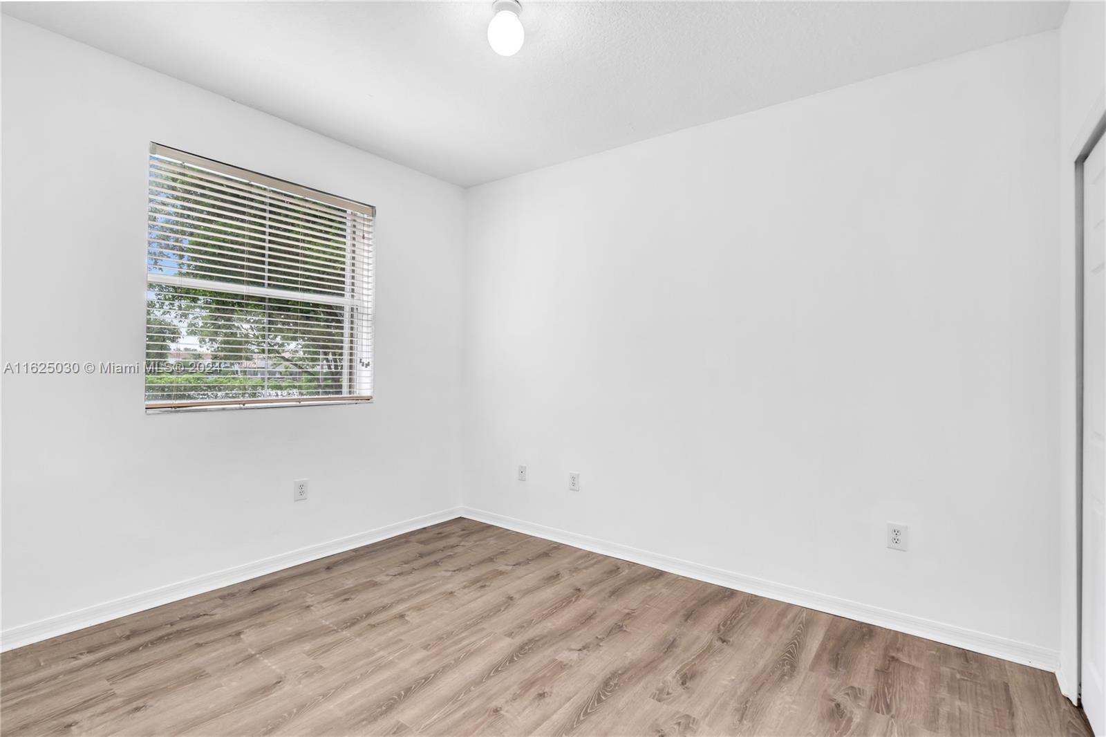 Empty room with wood-look flooring, white walls, and a window with horizontal blinds.