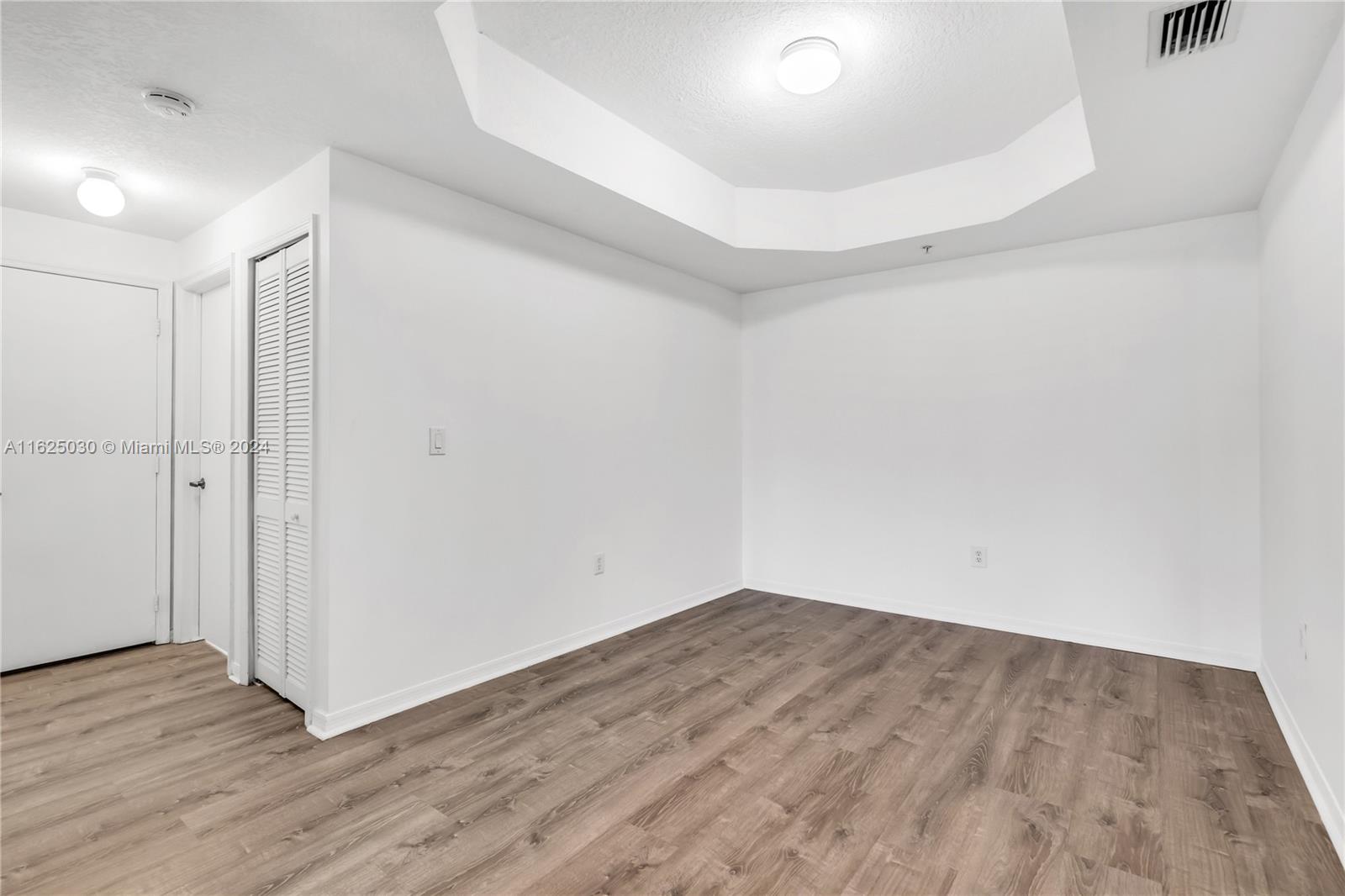 Empty bedroom with wood-look flooring, a tray ceiling, and a louvered closet door.