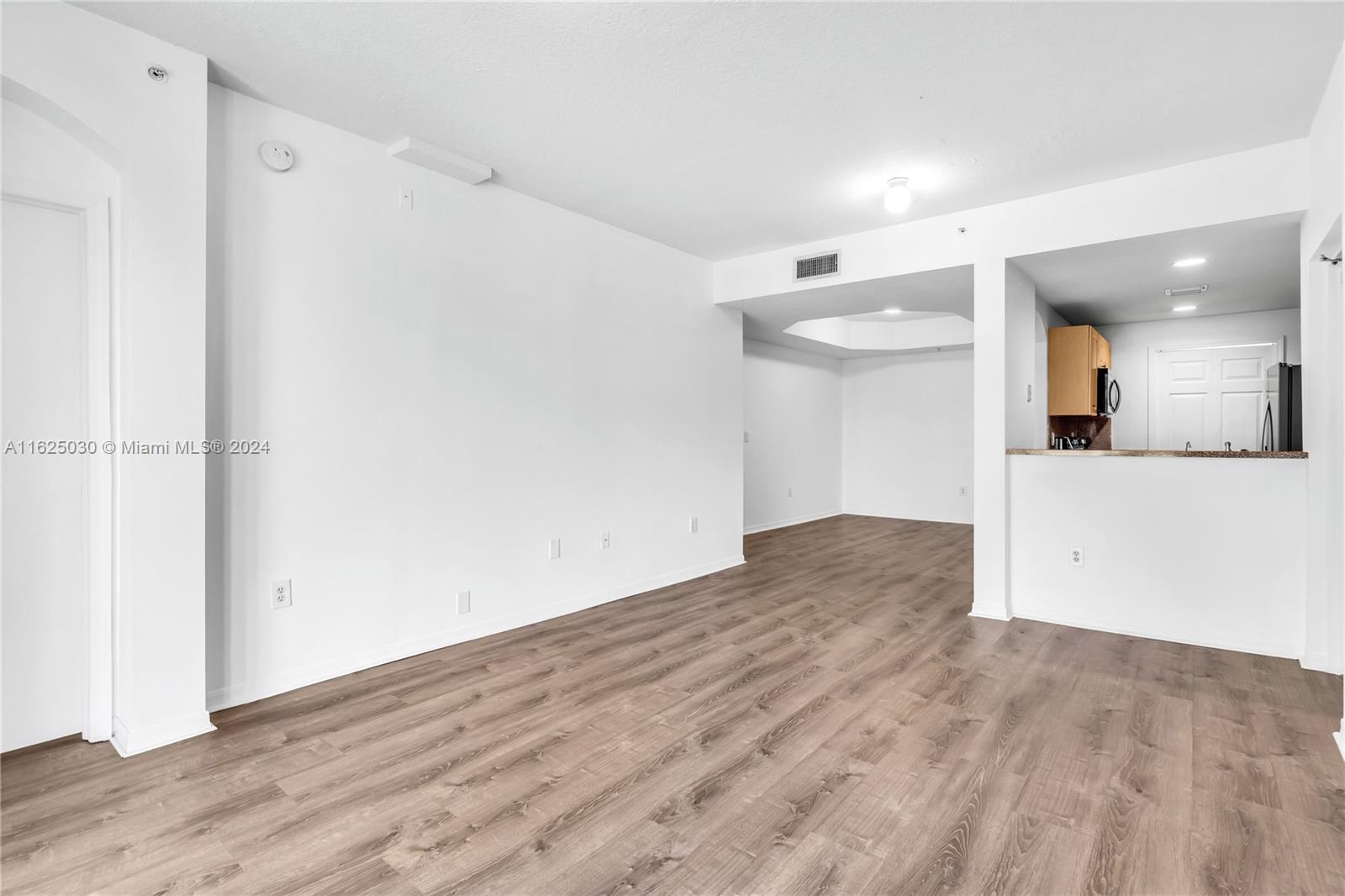 Unfurnished living and dining area with wood-look flooring and an open pass-through to the kitchen.