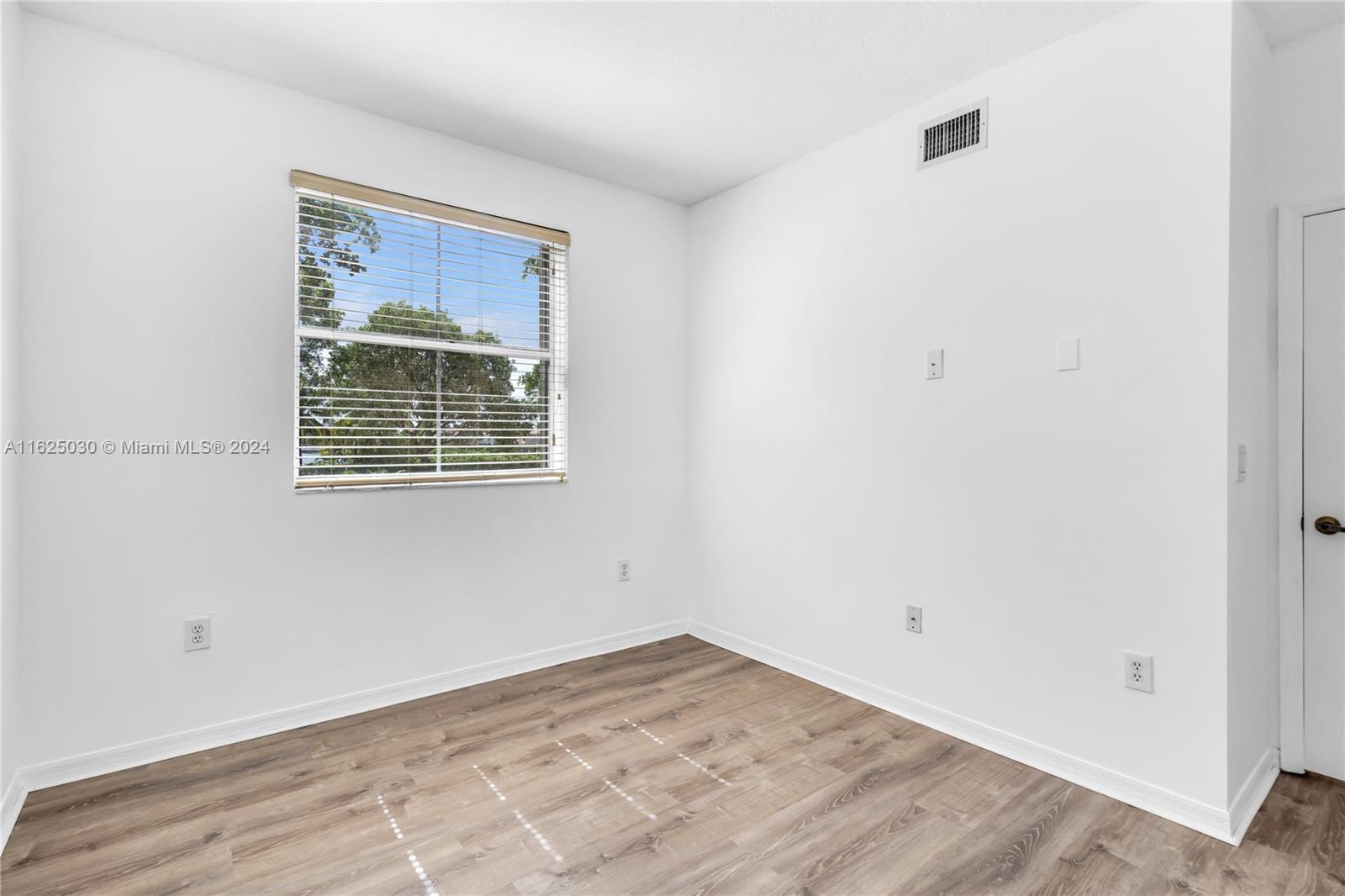 Empty bedroom with wood-look floors and a window with horizontal blinds.