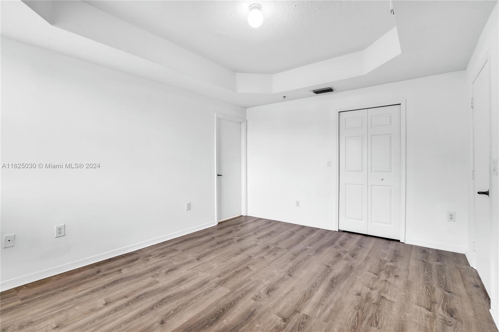 Vacant room with wood-look flooring, white walls, and closet doors.