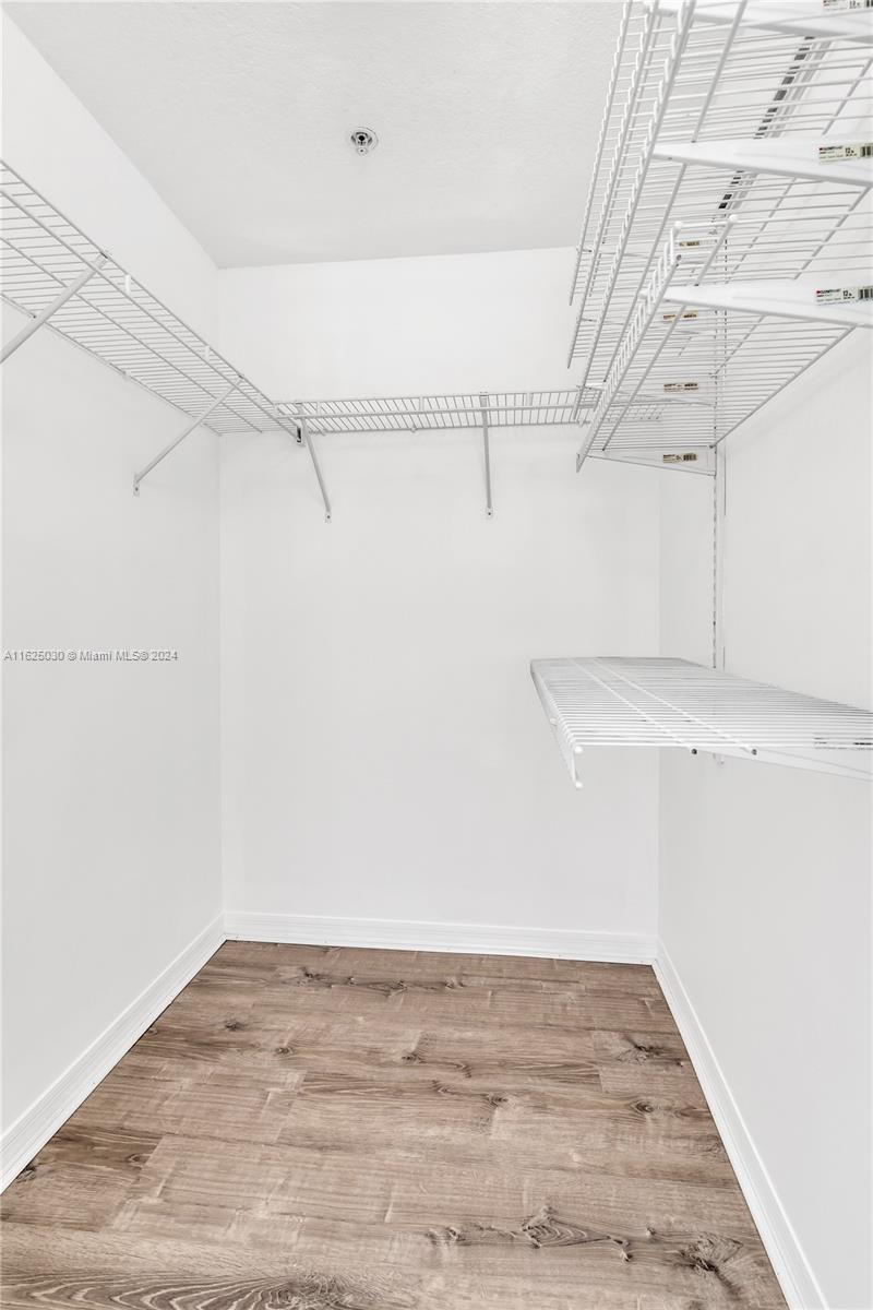 Empty walk-in closet with extensive white wire shelving and wood-look plank flooring.