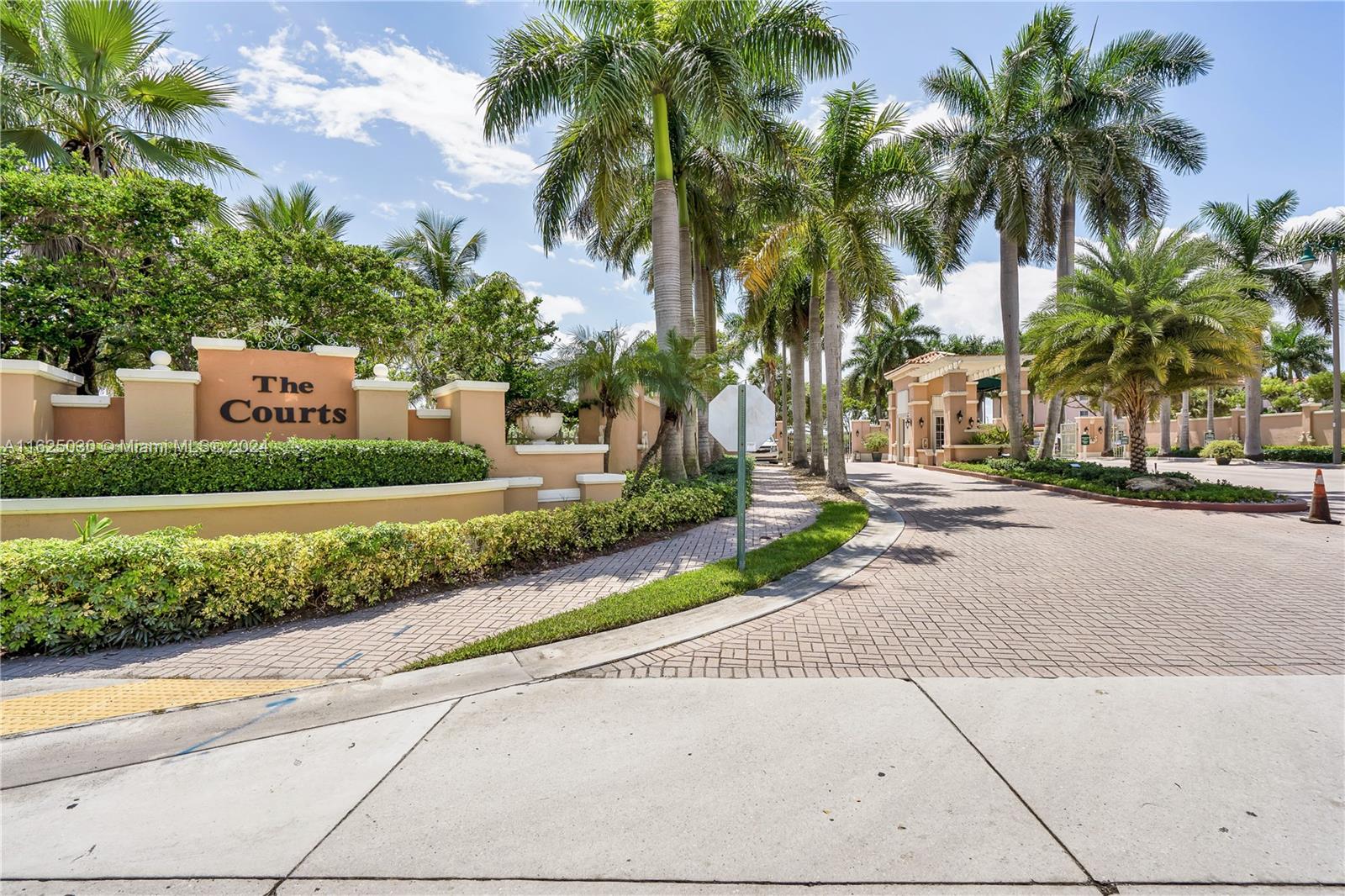 Entrance to The Courts residential community, with palm trees and a paved drive.