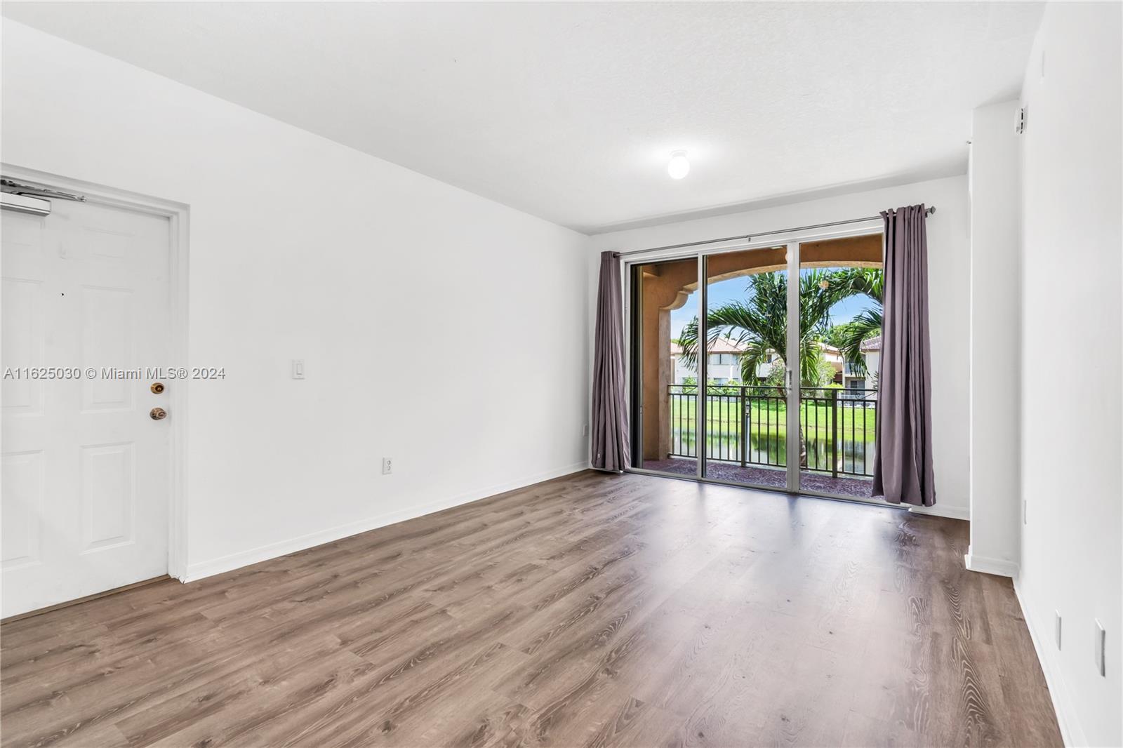 Empty living room with wood-look floors and sliding doors to a canal-view balcony.