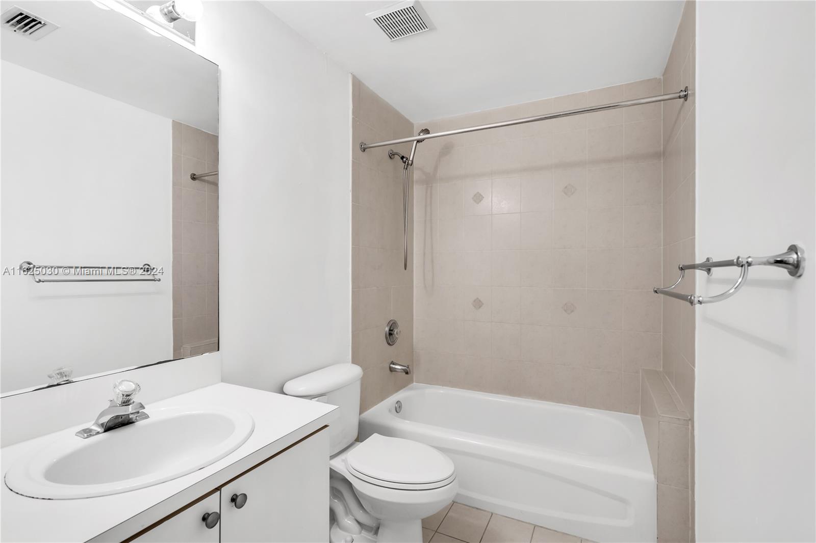 Bathroom with a white vanity, large mirror, and tub with beige tile surround.