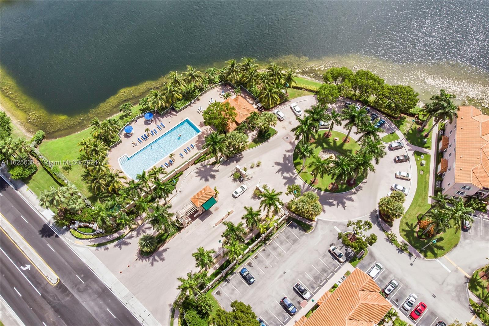 Aerial view of a lakeside condominium complex with a swimming pool and palm-lined grounds.