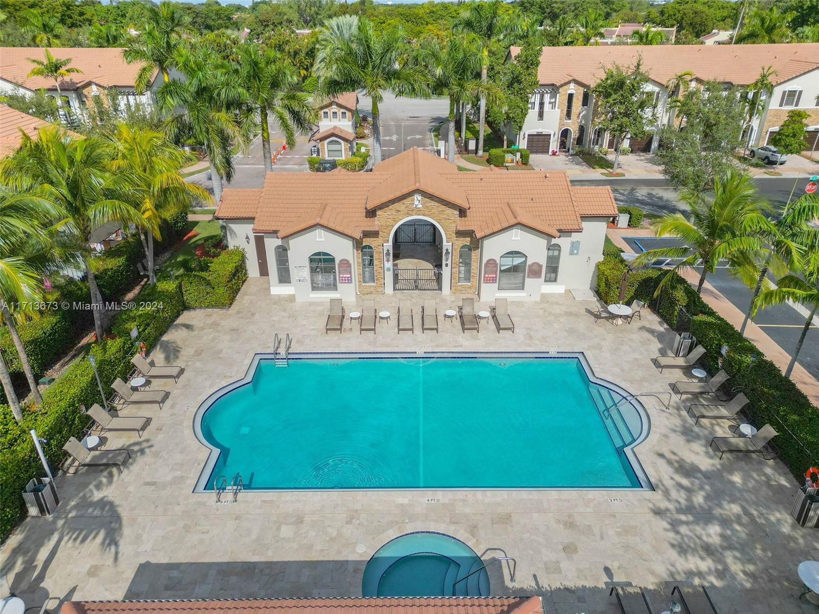 Aerial view of a turquoise community pool with a tiled deck, lounge chairs, and palm trees.