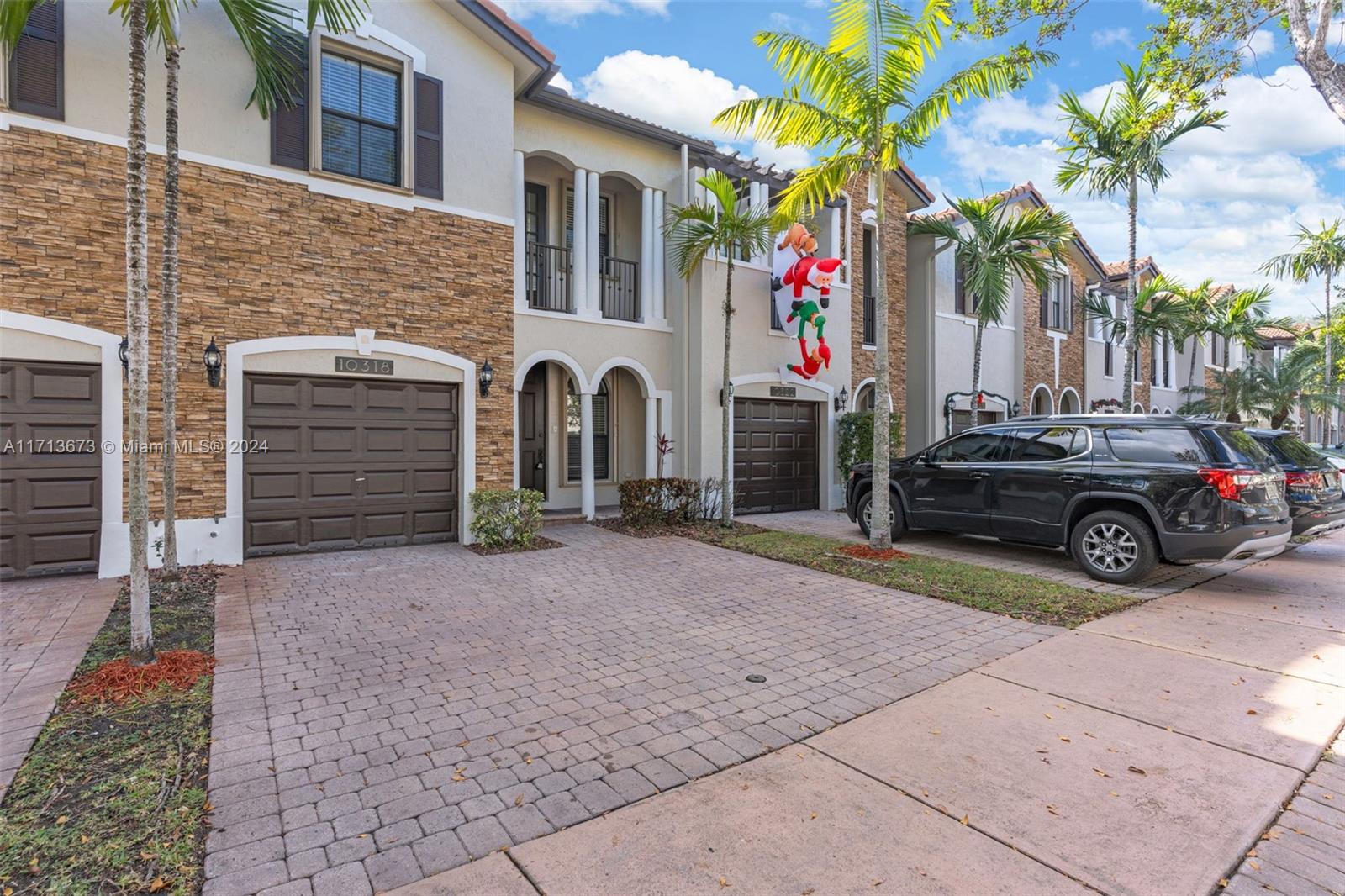 Townhouse exterior with stone veneer, a paved driveway, palm trees, and a hanging Santa decoration.