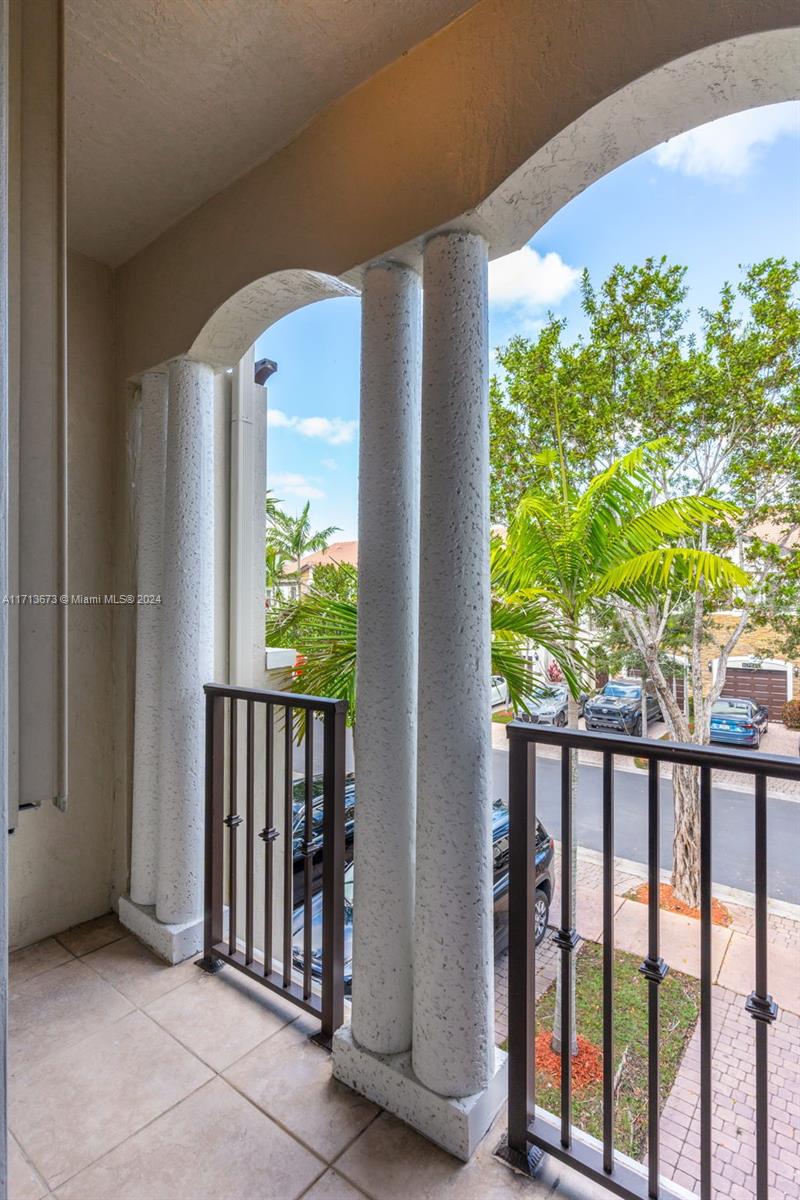 Tiled balcony with arched openings and columns overlooking a tree-lined street.