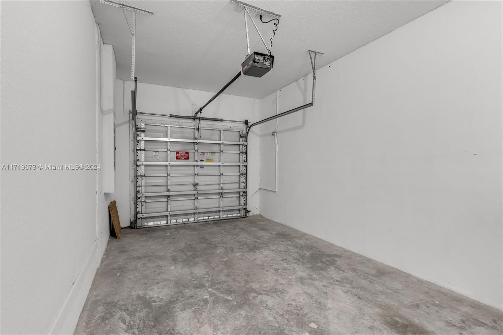 Empty garage with a concrete floor, closed sectional door, and overhead opener.