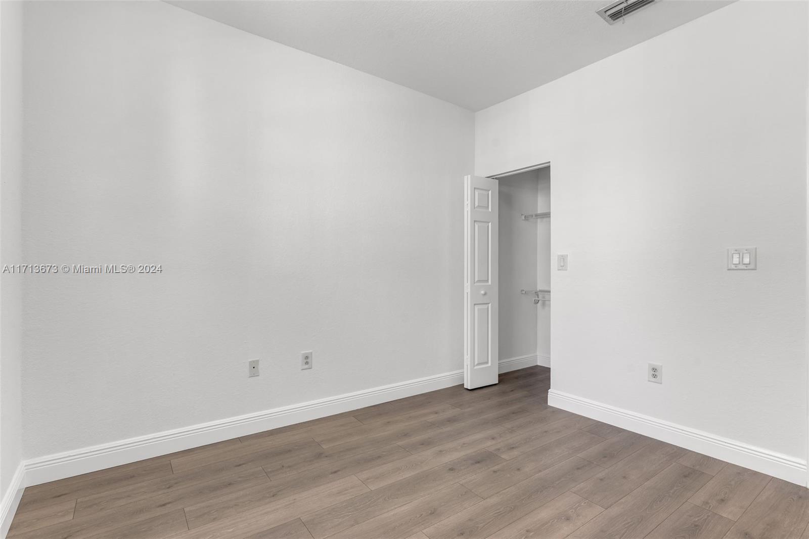 Empty bedroom with plank flooring and an open closet.