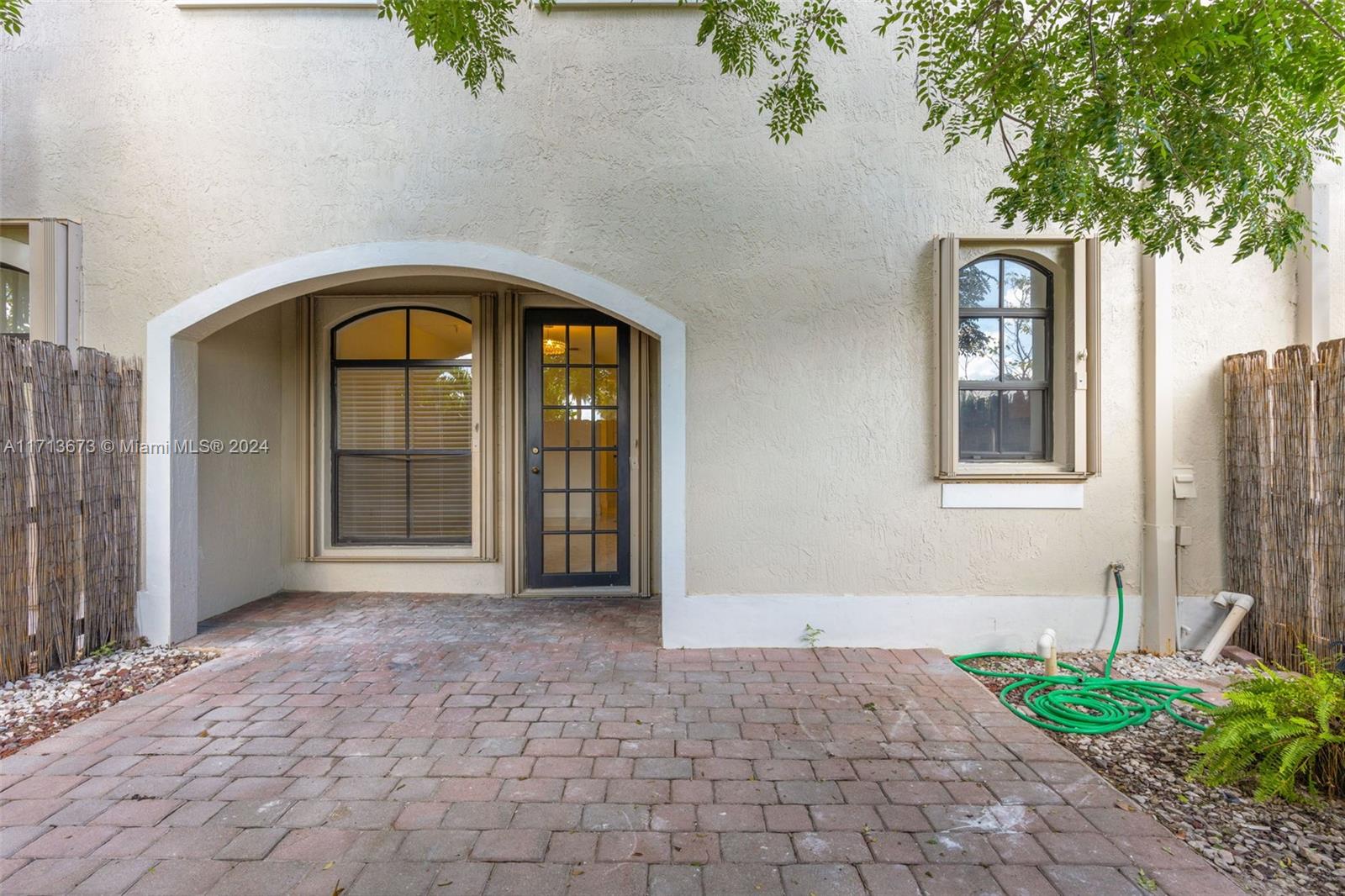 Home entrance with an arched entry, black glass-paneled door, and brick-paver courtyard.