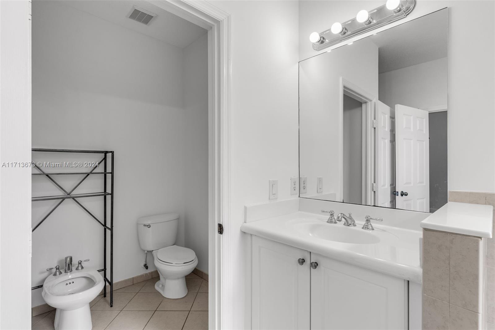 Bathroom with a white vanity and large mirror, plus a toilet and separate bidet.