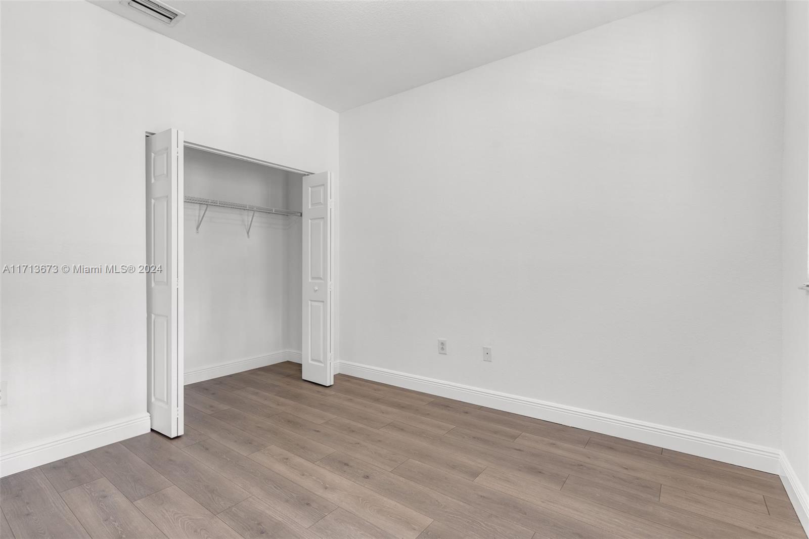 Empty bedroom with wood-look flooring and an open closet.