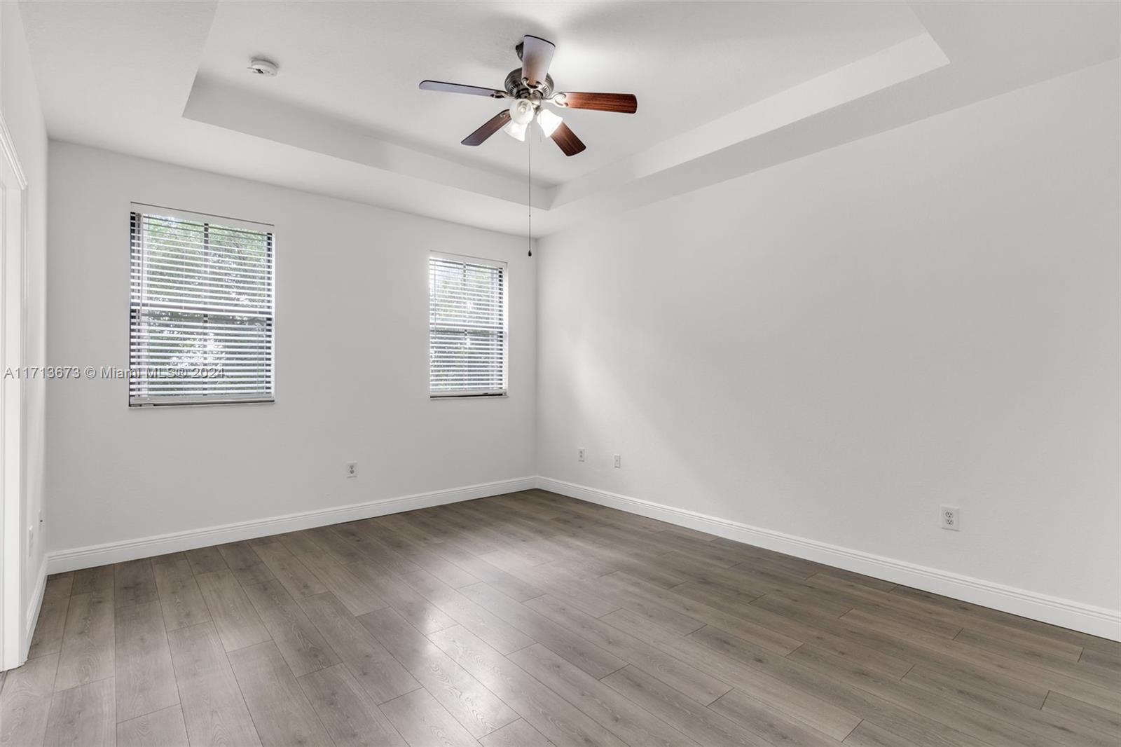 Empty bedroom with gray wood-look flooring, two blinded windows, and a ceiling fan with light.