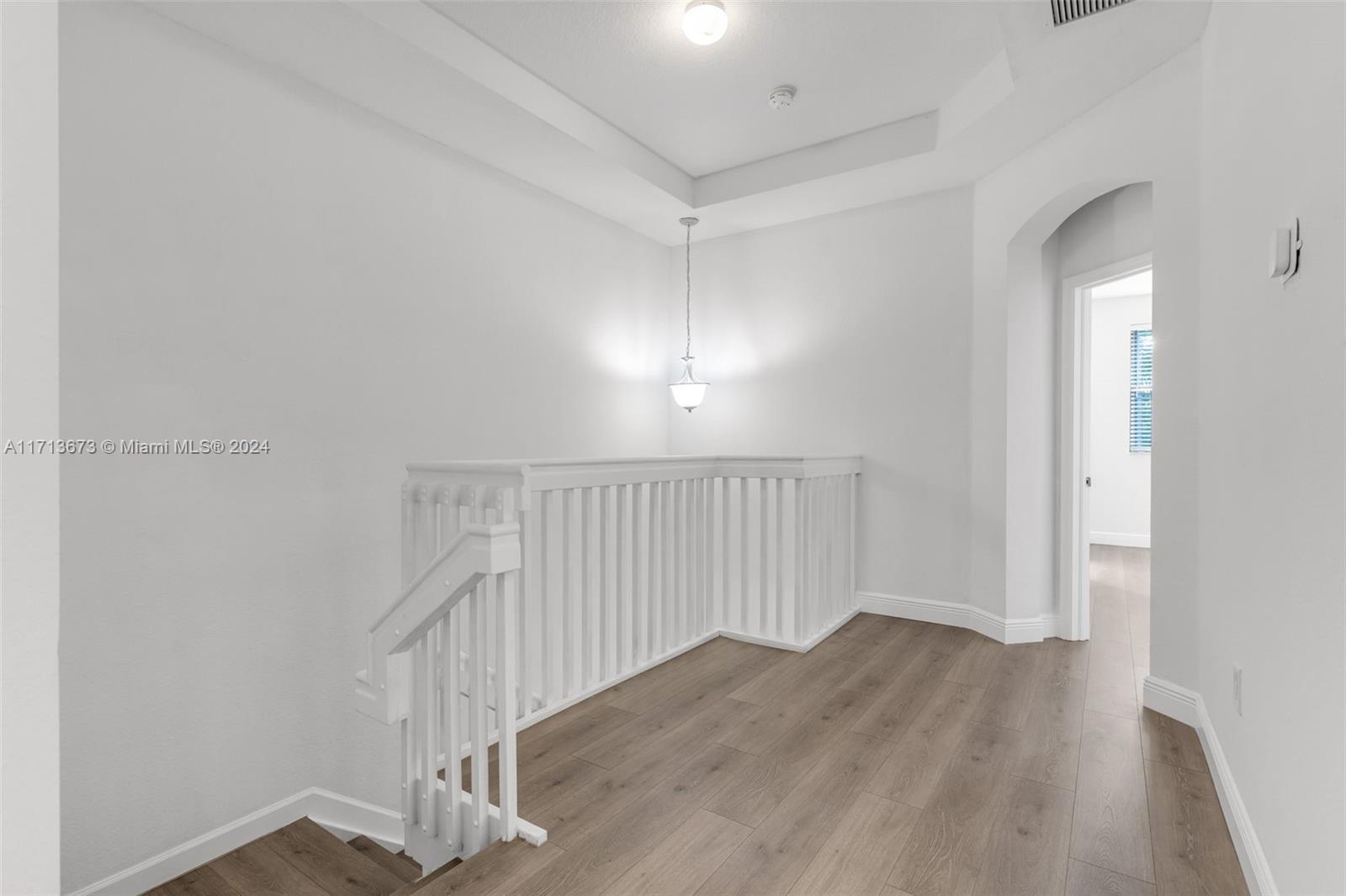 Upstairs landing with white stair railing, wood-look flooring, and an arched doorway.