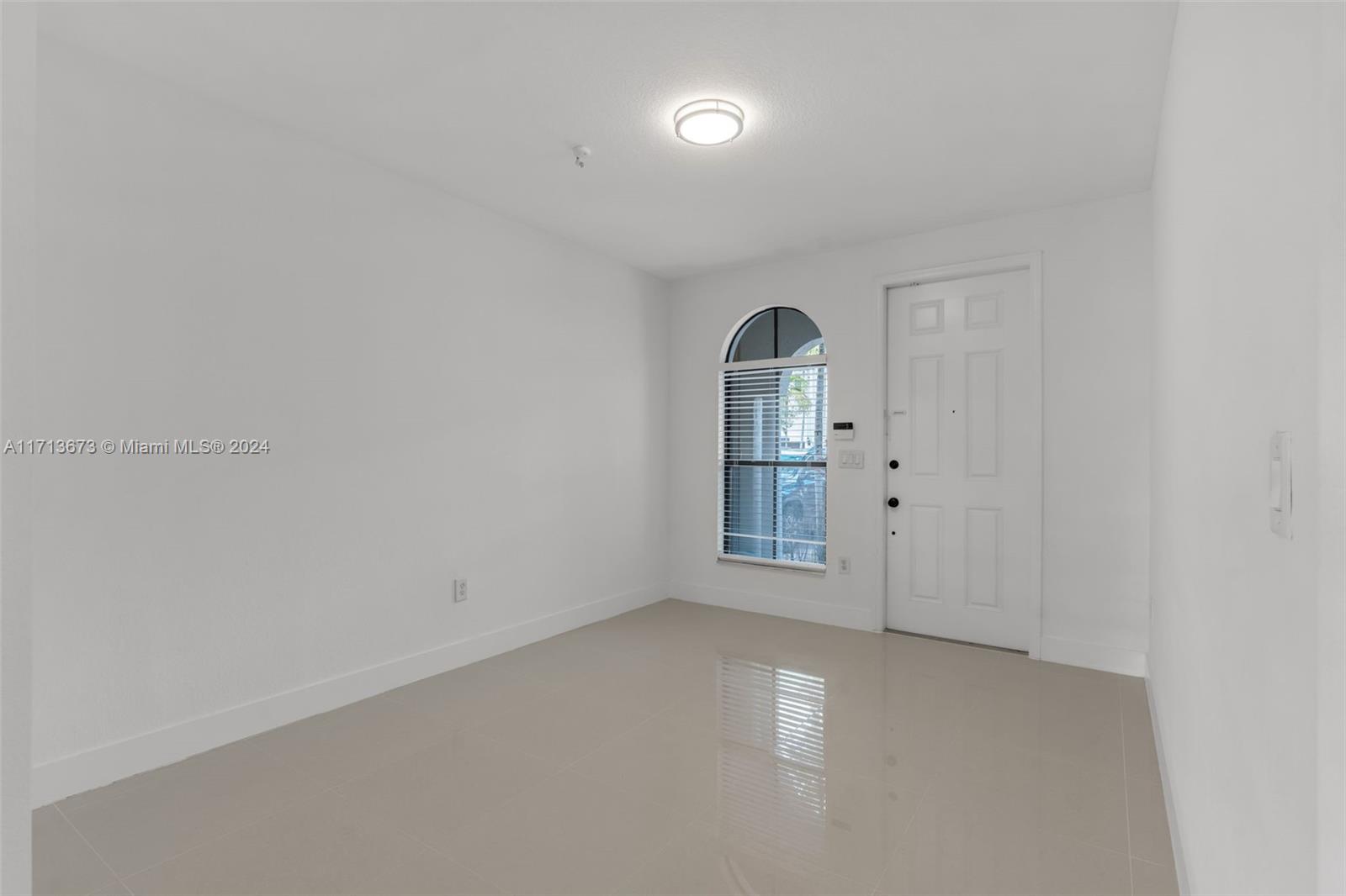 Empty entry with glossy tile floors, a white front door, and an arched window with blinds.