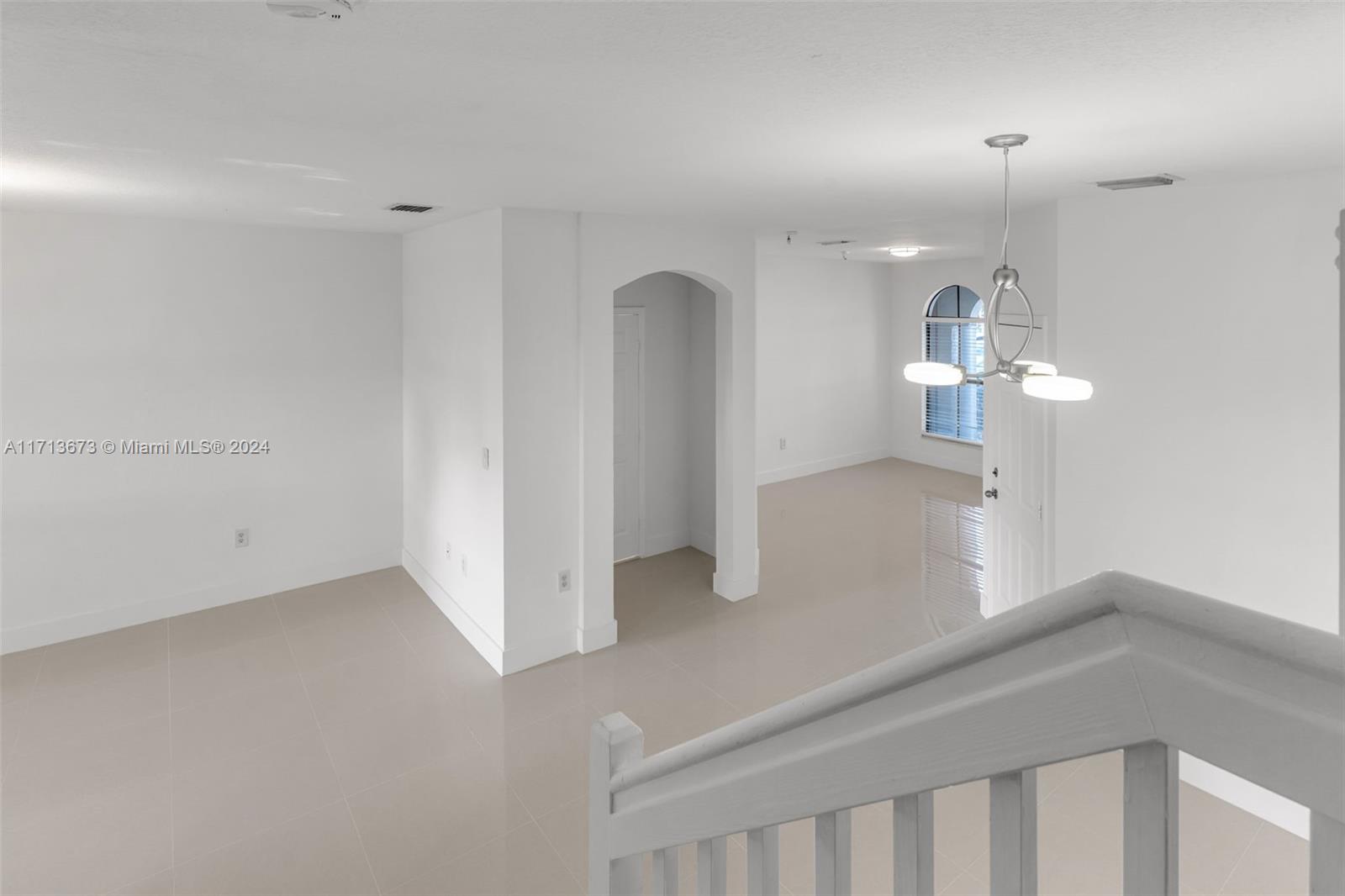 Vacant tiled living area with an arched opening, arched window, and pendant light.