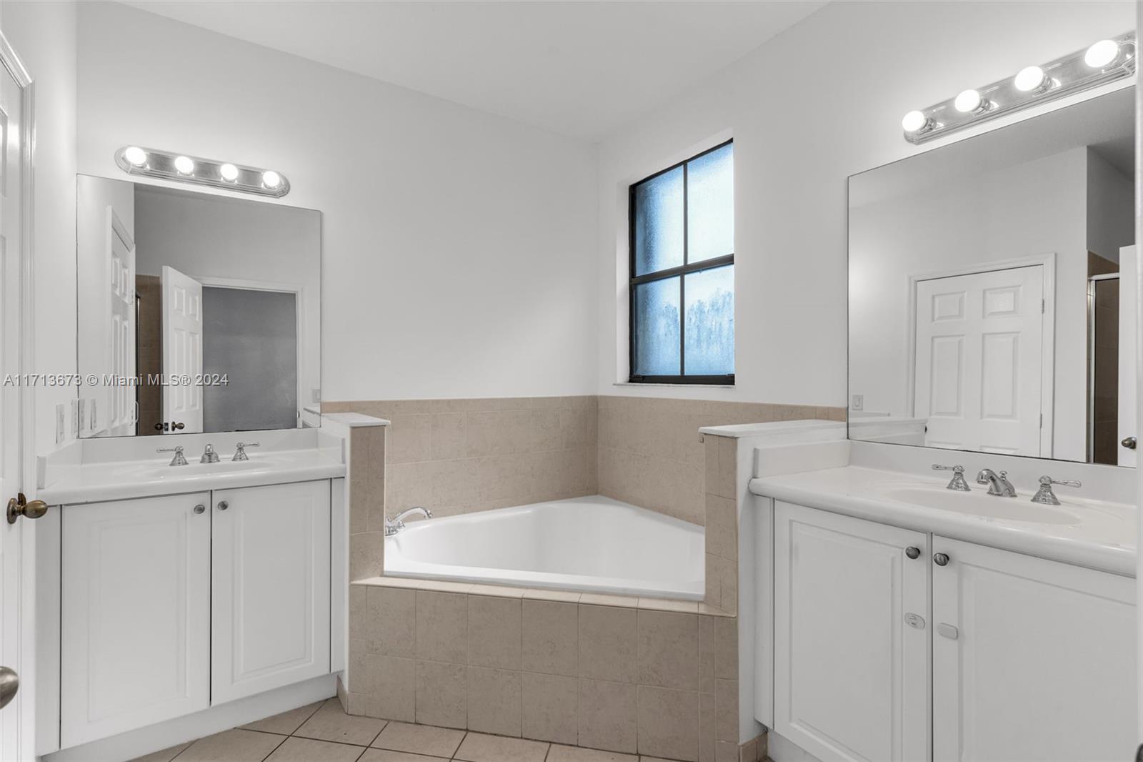 Bathroom with a corner soaking tub, beige tile surround, and white dual-sink vanities.