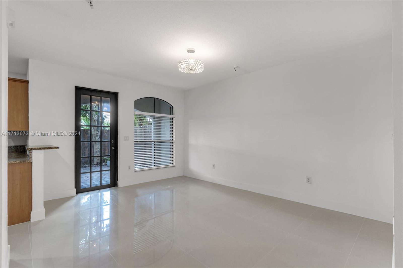 Vacant living area with glossy tile floors, black-framed glass door, and arched window with blinds.