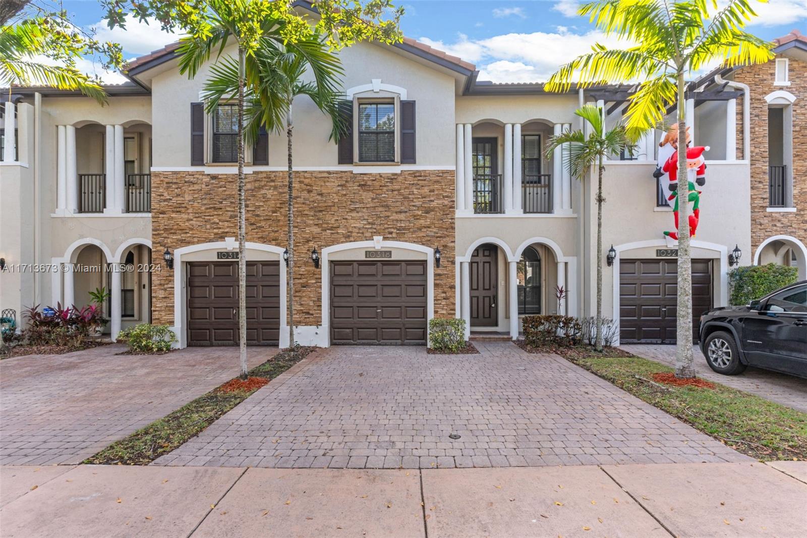 Townhouse exterior with stone facade, palm trees, paver driveway, and a Santa decoration on a neighboring unit.
