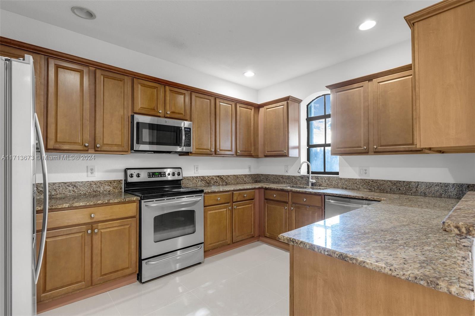 Kitchen with wood cabinets, granite counters, stainless steel appliances, and an arched window above the sink.