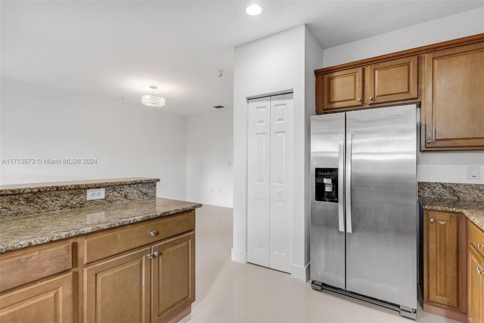 Kitchen with granite counters, honey-colored cabinets, and a stainless steel side-by-side refrigerator.
